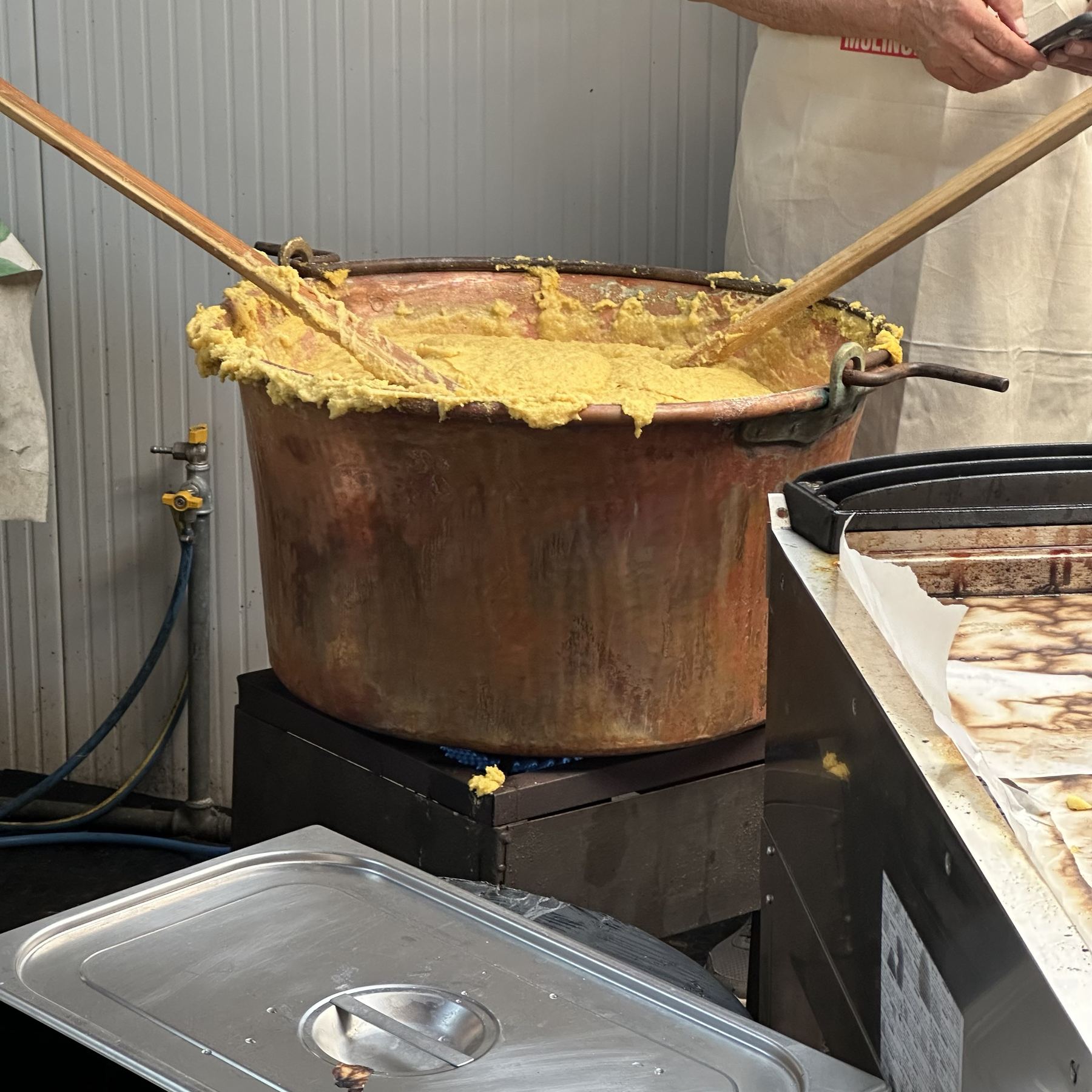 Polenta wordt geroerd in een grote koperen ketel boven het vuur